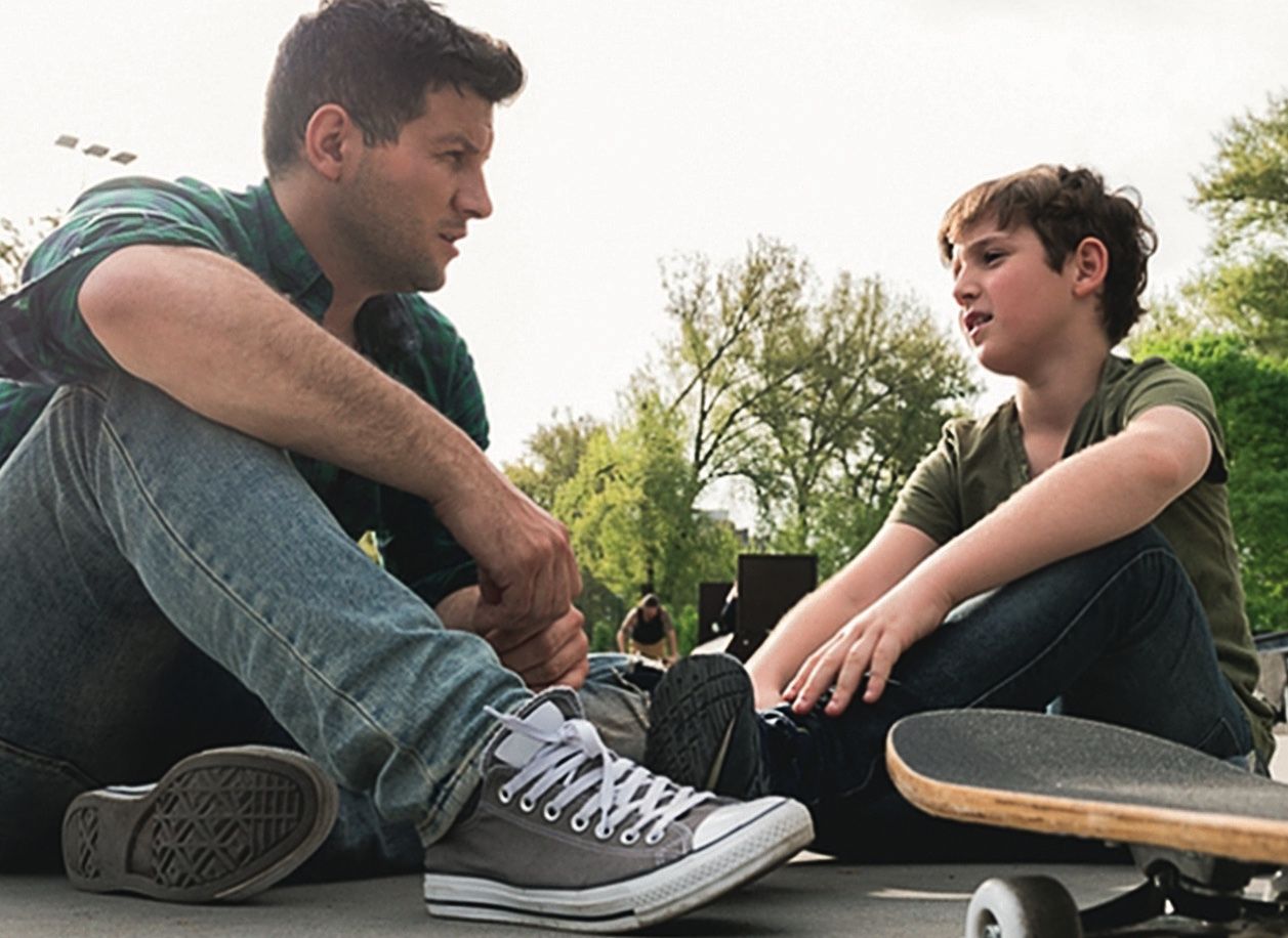 Junger Mann und Jugendlicher sitzen mit Skateboard zusammen und reden