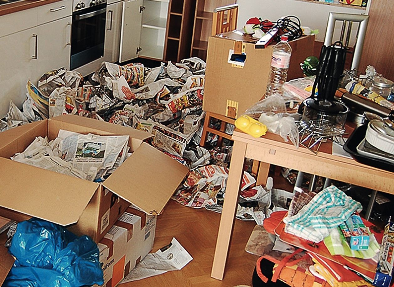 Unaufgeräumte Küche mit Kartons, Zeitungen und Taschen auf dem Boden